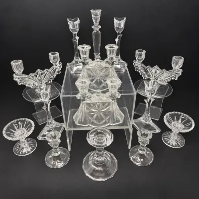 Sale Photo Thumbnail #36: Collection of vintage clear pressed and cut glass candlesticks, candelabras, and trinket boxes arranged on clear acrylic risers.