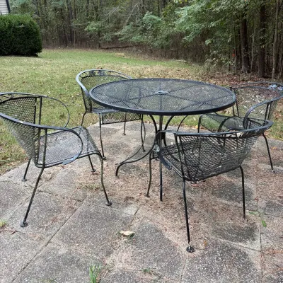Sale Photo Thumbnail #150: Black wrought iron patio dining set including a round mesh table with umbrella hole and four matching mesh armchairs, displaying light surface wear.