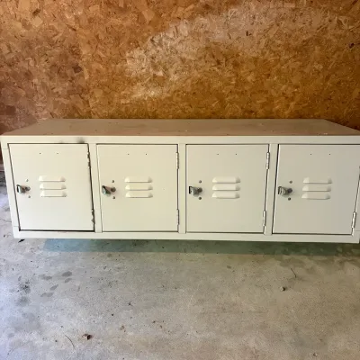 Sale Photo Thumbnail #113: Off-white metal four-door low storage locker unit with louvered vents and latch handles, featuring a flat top surface.