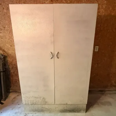 Sale Photo Thumbnail #111: Tall, white two-door storage cabinet featuring metal handles, showing significant surface wear and staining near the base.