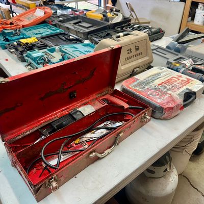 Sale Photo Thumbnail #24: Vintage Milwaukee Sawzall reciprocating saw inside a worn red metal carrying case, surrounded by various power tools in hard plastic cases.