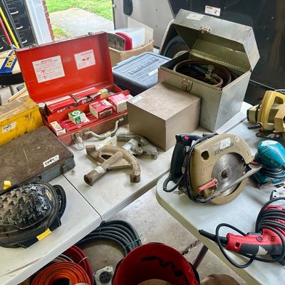 Sale Photo Thumbnail #12: Assortment of power tools, hand tools, and metal toolboxes arranged on folding tables, including a Skilsaw circular saw and conduit bender.