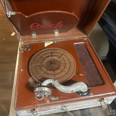 Sale Photo Thumbnail #43: Vintage Brock portable hand-crank phonograph housed in a brown carrying case, featuring a metal tonearm and textured turntable platter.