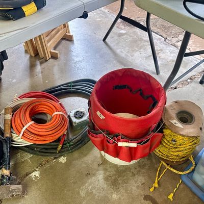 Sale Photo Thumbnail #13: Collection of workshop supplies including a red canvas bucket tool organizer, coiled extension cords and wire, a spool of yellow rope, and a sledgehammer.