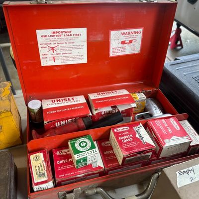 Sale Photo Thumbnail #3: Vintage red metal Uniset stud driver kit complete with the powder-actuated tool, warning labels, and assorted boxes of drive pins and powder loads.