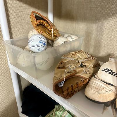 Sale Photo Thumbnail #47: Collection of used baseball gear including a bin of baseballs and softballs, leather gloves, and Mizuno cleat-style shoes on a plastic shelf.