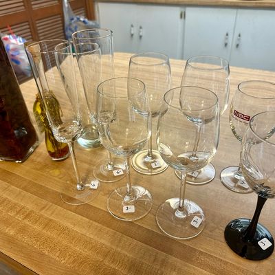 Sale Photo Thumbnail #65: Assortment of clear glass stemware, including wine glasses and champagne flutes, displayed on a wooden countertop.