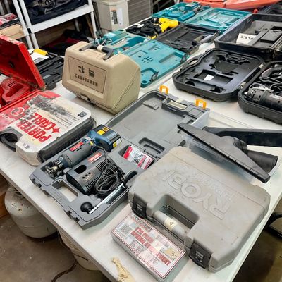 Sale Photo Thumbnail #23: An assortment of power tools and plastic carrying cases arranged on folding tables, including Ryobi, Porter-Cable, and Craftsman brands.