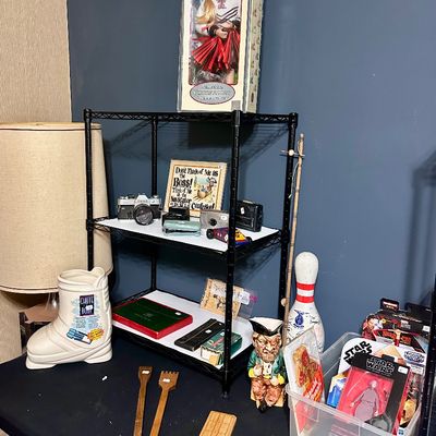 Sale Photo Thumbnail #31: Collection of eclectic vintage items including a boxed Texas Tech cheerleader doll, cameras, action figures, a ceramic boot, and wooden accessories displayed on shelving.