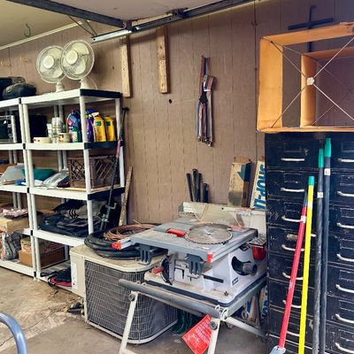 Sale Photo Thumbnail #7: Workshop storage setup featuring plastic shelving units filled with household items, a table saw, an outdoor AC compressor unit, and a tall metal filing cabinet.