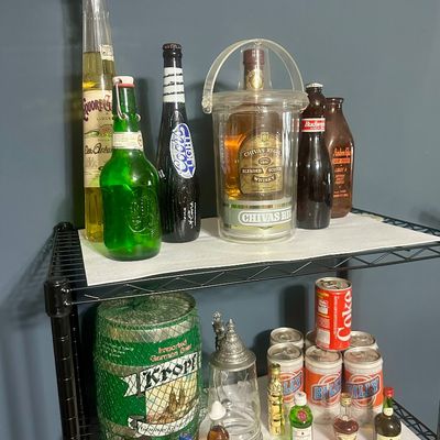 Sale Photo Thumbnail #51: Collection of vintage liquor and beer bottles, novelty cans, and barware arranged on a wire shelving unit.