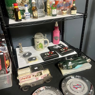 Sale Photo Thumbnail #52: Wire shelving unit displaying vintage collectible items, including miniature liquor bottles, Billy Beer cans, a vintage Coca-Cola delivery truck toy, and chrome Cadillac hubcaps.