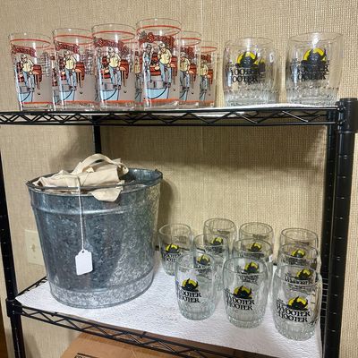 Sale Photo Thumbnail #44: Collection of Jack Daniel's promotional glassware, including 'Bung Slinger' highball glasses and 'Wyooter Hooter' lowball glasses, alongside a galvanized metal bucket.