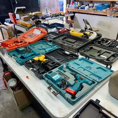 Sale Photo Thumbnail #25: Large collection of power tools and molded carrying cases arranged on a folding table, including Makita cordless drills, a DeWalt band saw, and orange Ridgid tools.