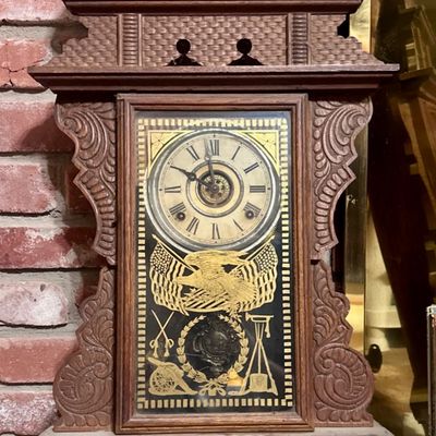 Antique carved oak gingerbread mantle clock with decorative glass door featuring an eagle and military motifs.