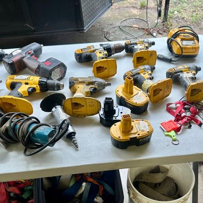 Sale Photo Thumbnail #14: Assortment of power tools, including DeWalt cordless drills, impact drivers, chargers, batteries, and a Makita angle grinder on a plastic folding table.