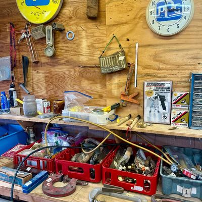 Sale Photo Thumbnail #10: Workshop wall filled with vintage PPG clocks, caulk guns, C-clamps, pry bars, and various hardware accessories organized on shelves and in crates.