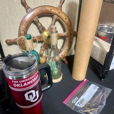 Sale Photo Thumbnail #45: Collection of decor items including a University of Oklahoma insulated travel mug, a wooden ship's wheel, decorative glass bottles, and a poster tube.