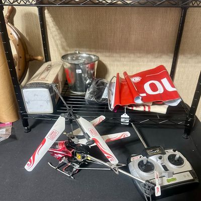 Sale Photo Thumbnail #46: Remote control toy helicopter with handheld transmitter alongside assorted household items on wire shelving.