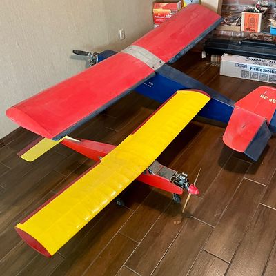 Two gas-powered radio-controlled model airplanes, including a large red and blue model marked RC 48 and a smaller red and yellow trainer.