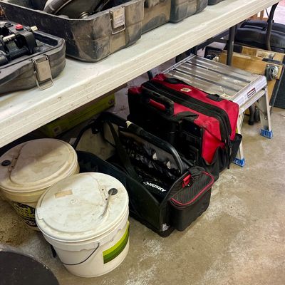 Sale Photo Thumbnail #22: Collection of workshop equipment including tool bags, hard plastic cases, plastic buckets, and a small aluminum step stool under a folding table.
