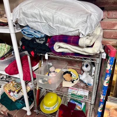 Sale Photo Thumbnail #34: Wire shelving unit holding folded blankets, a pillow, plush toys, plastic storage bins, and a yellow Year 2000 party hat.
