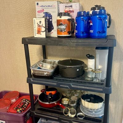 Sale Photo Thumbnail #55: Black plastic four-tier shelving unit filled with assorted kitchenware, including insulated drink jugs, cast iron cookware, canning jars, and storage containers.