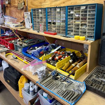 Sale Photo Thumbnail #9: Workshop bench loaded with assorted hand tools, including pry bars, hammers, socket sets, and three wall-mounted plastic parts organizer cabinets.