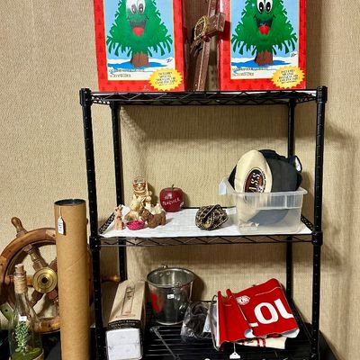 Sale Photo Thumbnail #36: Black wire shelving unit displayed with novelties including vintage boxed Douglas Fir talking Christmas trees, baseball caps, and a remote-controlled helicopter.