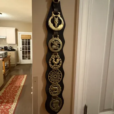 Sale Photo Thumbnail #15: Vintage English brass horse brasses mounted on a long black leather martingales strap, featuring various animal and geometric designs.