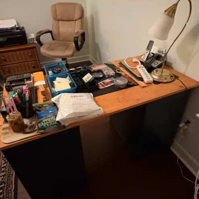 Sale Photo Thumbnail #68: Wooden top desk with black pedestal bases, featuring various office supplies, a gooseneck brass lamp, and a tan executive swivel chair in the background.