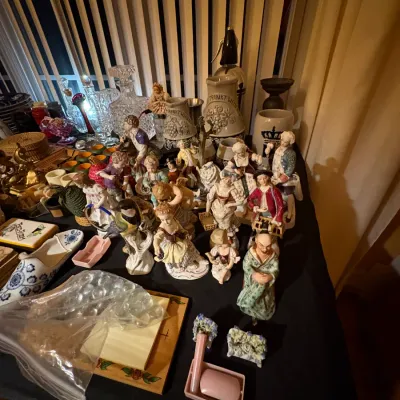 Sale Photo Thumbnail #10: Collection of vintage porcelain figurines, cut crystal decanters, and German stein jugs displayed on a table.
