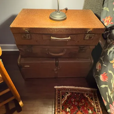 Sale Photo Thumbnail #77: Stack of three vintage brown hard-shell suitcases styled as a nightstand, topped with a small accent lamp.