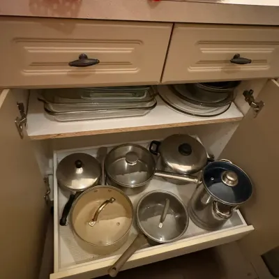 Sale Photo Thumbnail #41: Collection of assorted cookware, including stainless steel and non-stick pots, pans, and glass baking dishes organized in a kitchen cabinet.