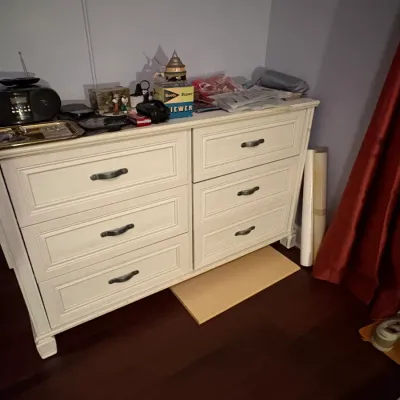 Sale Photo Thumbnail #76: Off-white six-drawer dresser with dark metal hardware, displaying various small household items and electronics on top.