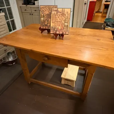 Sale Photo Thumbnail #44: Rustic pine kitchen island or work table featuring a single drawer and stretchers, displayed with decorative framed prints on top.