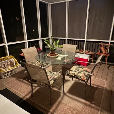Sale Photo Thumbnail #43: Outdoor patio set featuring a glass-top dining table with a stone pedestal base and four metal armchairs with floral patterned seat cushions.