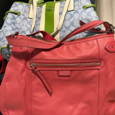 Sale Photo Thumbnail #14: Two Coach shoulder bags, including a coral pink leather hobo bag in the foreground and a blue Jacquard canvas signature tote with green trim in the background.