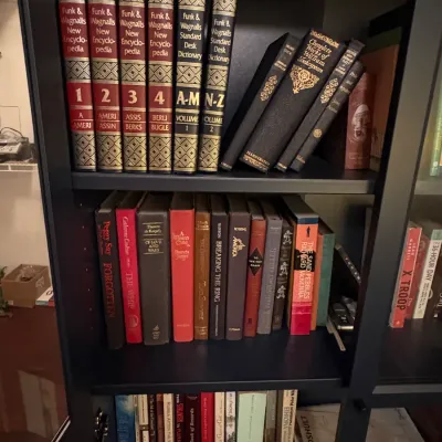 Sale Photo Thumbnail #65: Collection of hardbound books housed in a black bookcase, featuring volumes of Funk & Wagnalls encyclopedia and various literary titles.
