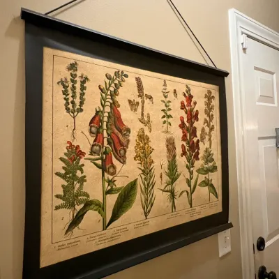 Sale Photo Thumbnail #42: Vintage-style botanical print scroll featuring detailed illustrations of various flowering plants, suspended from a black wooden hanging frame.