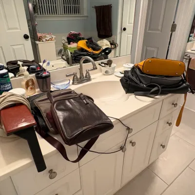 Sale Photo Thumbnail #57: Selection of leather and faux-leather handbags displayed on a bathroom vanity alongside personal care item