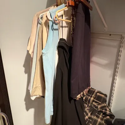 Sale Photo Thumbnail #60: Assorted women's clothing including tops, a black dress, and a plaid jacket hanging on a closet rack.
