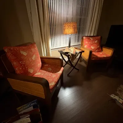 Sale Photo Thumbnail #23: Pair of wooden armchairs with woven cane sides and red pattern cushions, flanking a small folding butler table with an illuminated table lamp.