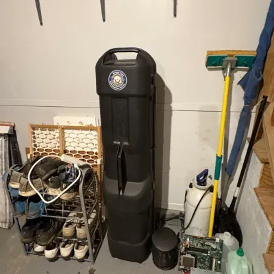 Sale Photo Thumbnail #49: Black hard-shell SKB golf bag travel case standing next to a shoe rack and cleaning supplies in a storage space.