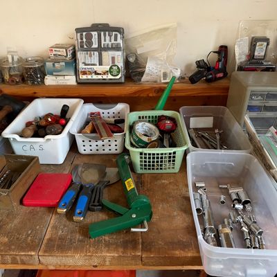 Sale Photo Thumbnail #11: Wooden workbench arranged with assorted hand tools, plastic storage bins containing socket sets, putty knives, a caulking gun, and glass jars filled with hardware.