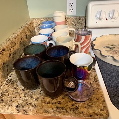 Sale Photo Thumbnail #86: Collection of assorted ceramic mugs, insulated tumblers, and a floral pie dish displayed on a kitchen countertop.