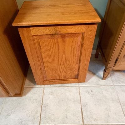 Sale Photo Thumbnail #2: Tilt-out wooden trash bin or hamper in light oak, featuring a paneled front and a round wood pull knob.