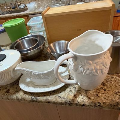 Sale Photo Thumbnail #82: Collection of assorted kitchenware including embossed white ceramic pitchers, stainless steel mixing bowls, plastic Tupperware canisters, and an OXO salad spinner.