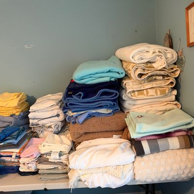 Sale Photo Thumbnail #31: Large assortment of folded bed linens, blankets, and towels organized in stacks on a folding table.
