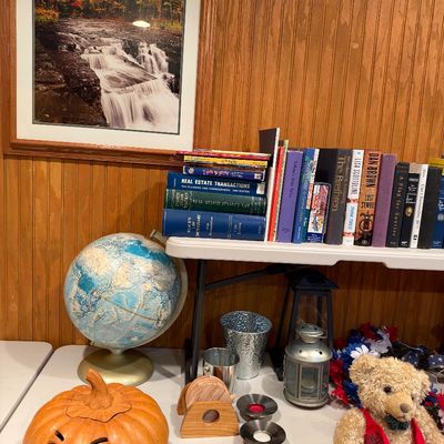 Sale Photo Thumbnail #103: Collection of home decor and books, including a desktop globe, jack-o'-lantern decor, teddy bear, small metal lanterns, and framed waterfall print.